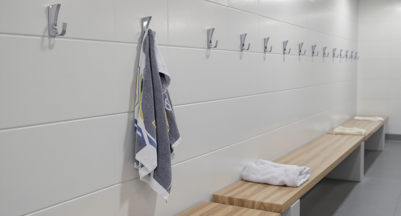 A clean, modern gym locker room scene with a towel hanging on a hook next to a shared bench, highlighting the risk of indirect contact transmission. Bright, clean lighting, stock photo style.